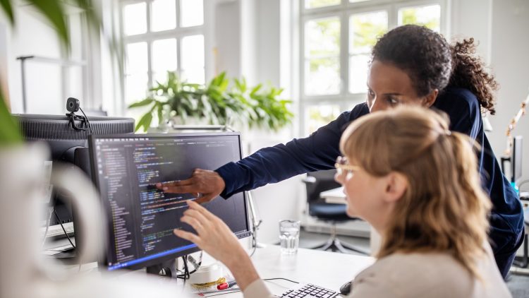 Two women discuss over code displayed on the computer screen
