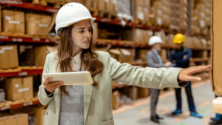 Getty Images - With a tablet in hand, a female warehouse owner walks through her busy warehouse. Dressed in smart business attire, reviewing logistics or inventory data. The spacious warehouse with neatly stocked shelves provides a clear view of the scale of the operation, emphasizing the owners hands-on approach to managing her business.