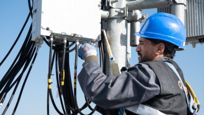 Technicien équipé d’un casque de sécurité installant et connectant des câbles sur un équipement télécom en hauteur.
