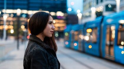 Young woman waiting for a tram in an urban environment at dusk.